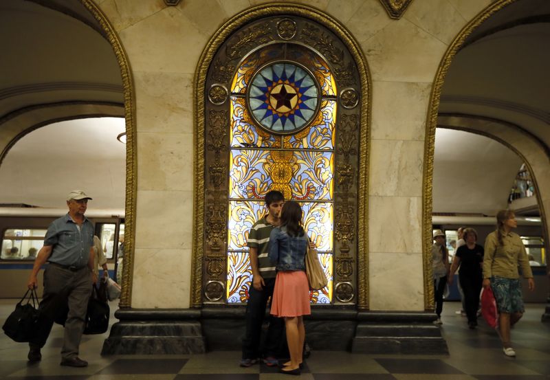 Couple kisses in front of a stained glass panel in Novoslobodskaya metro station in Moscow