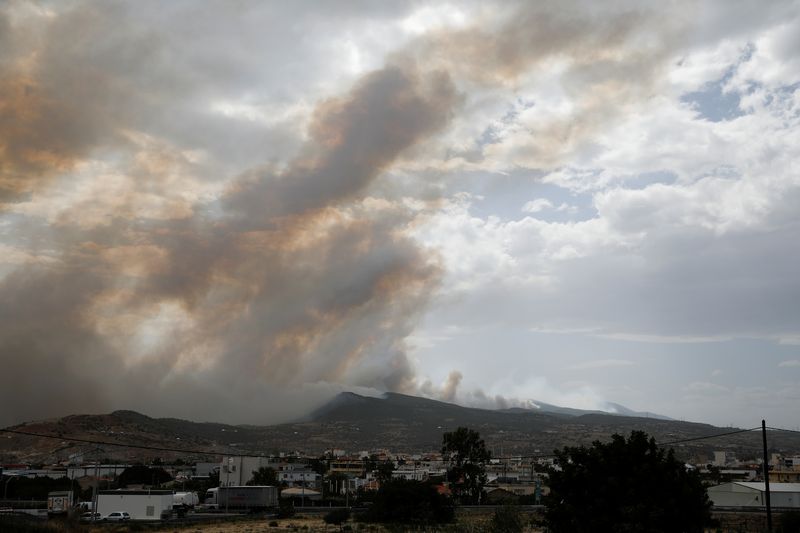 A village is seen amid smoke as a wildfire burns in Kineta
