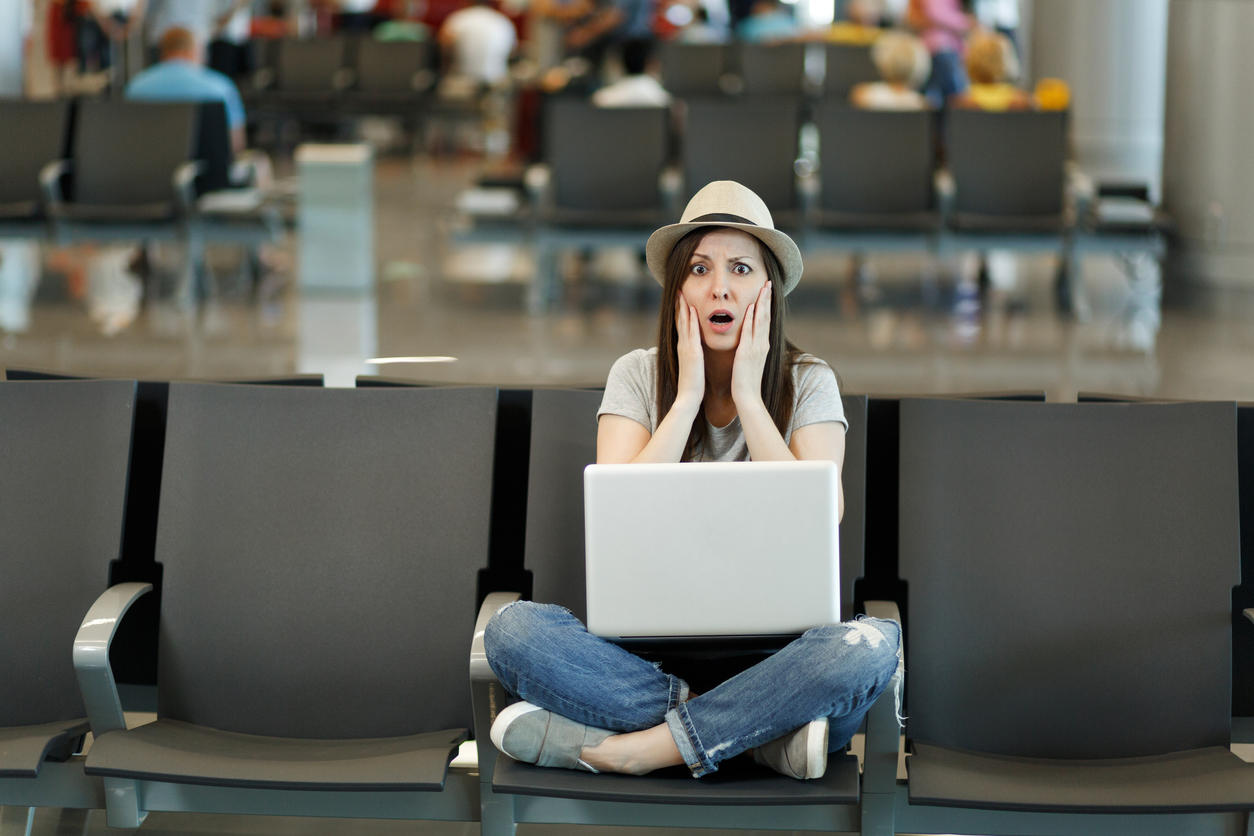 Scared traveler tourist woman with laptop sitting with crossed legs, clinging to face, waiting in lobby hall at airport. Passenger traveling abroad on weekends getaway. Air flight, overbooking concept