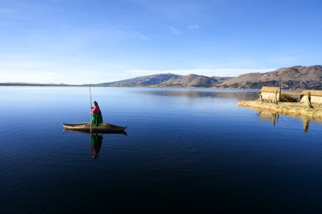 Woman wearing traditional costume, using traditionally made reed boat. The Uros Islands, Lake Titicaca. Puno. Peru.