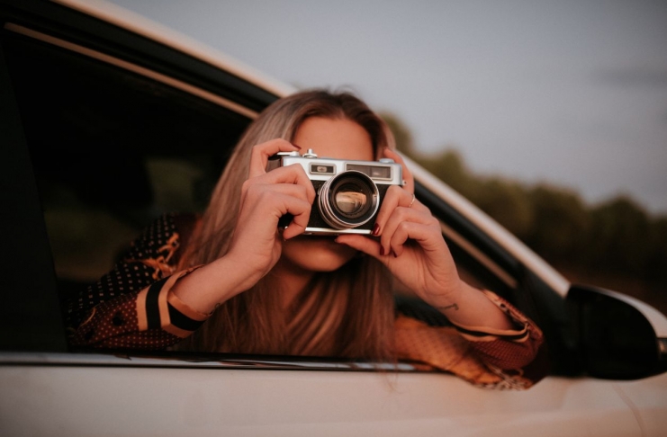 Young woman taking a picture with a vintage camera from car window
